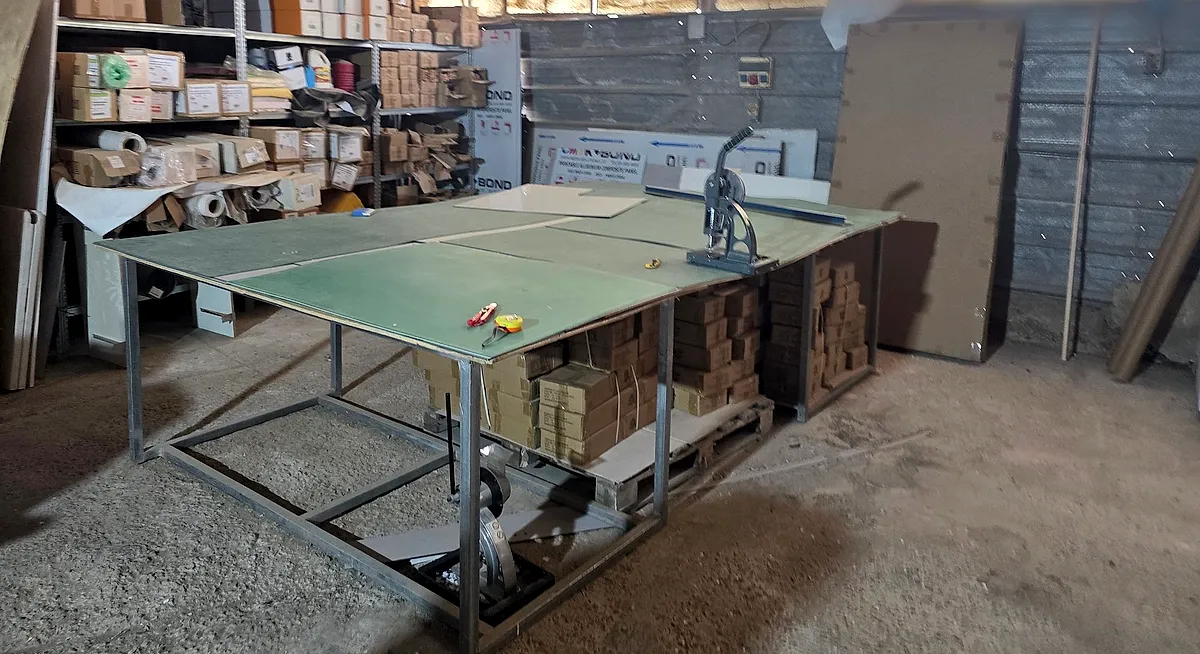 שולחן חיתוך והרכבה גדול ומדפי חומרי גלם מאחוריו