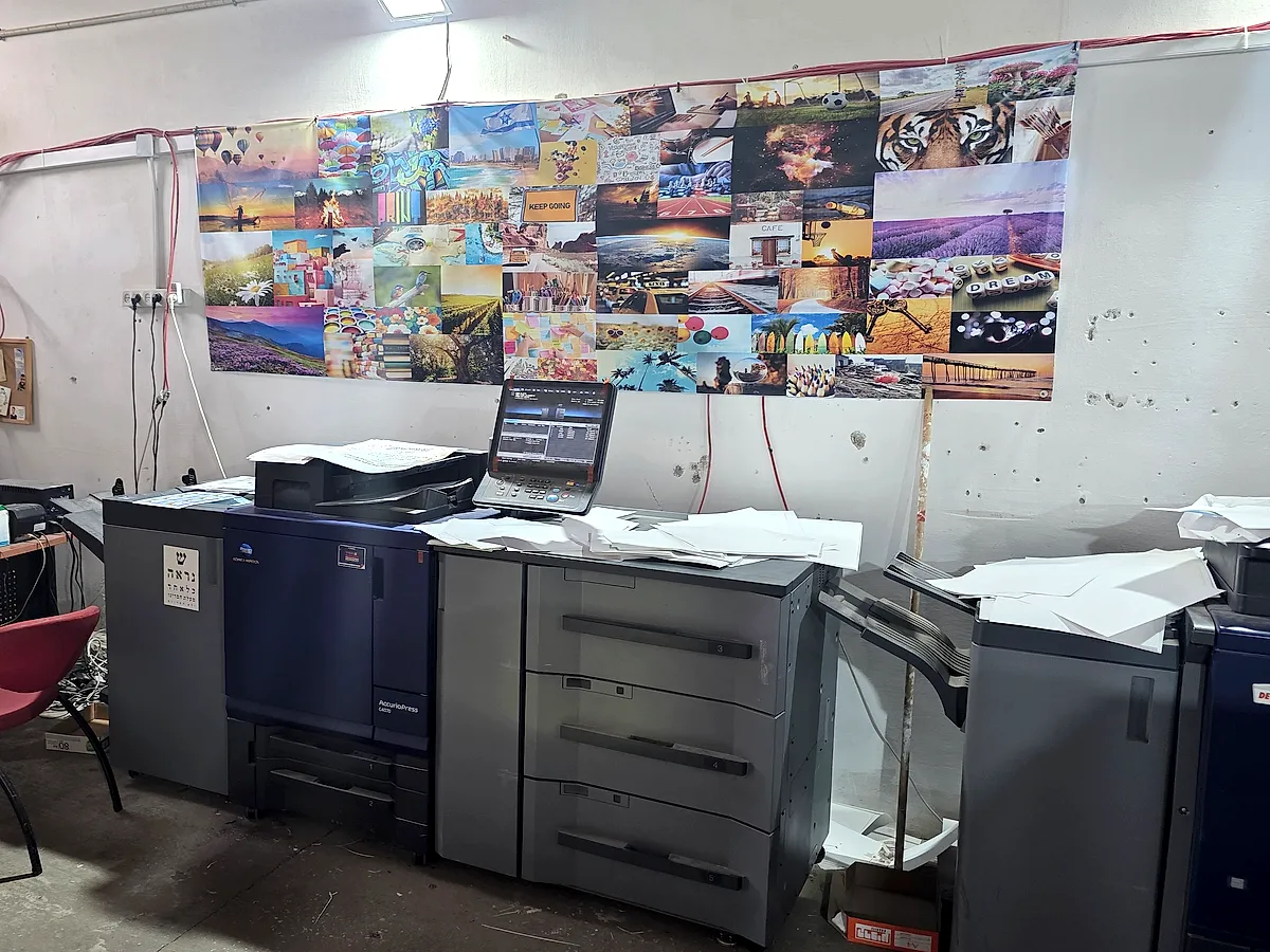 מכונת דפוס דיגיטלית בדפוס, ומולה קיר עם תמונות מודפסות